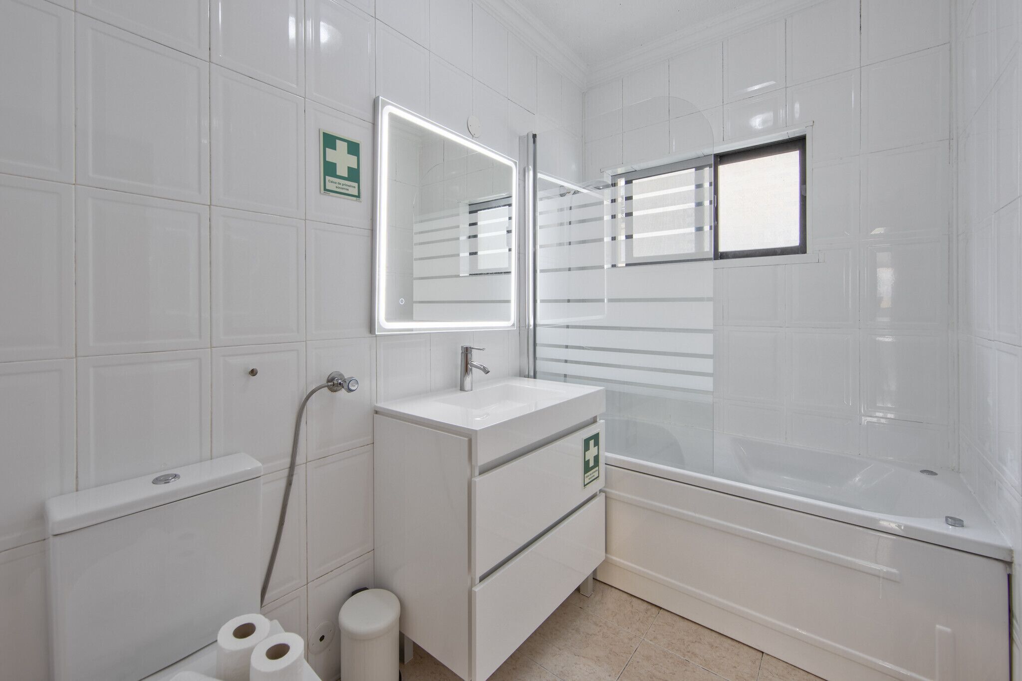 Un baño moderno con azulejos blancos, un espejo grande, un lavabo, un inodoro y una bañera.