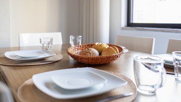 Een eettafel gedekt met borden, een broodmand en glazen.