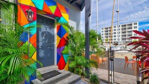 Een kleurrijk gebouw met een geometrisch gevelontwerp, een deur met de aanduiding '2', en een uitzicht op een jachthaven met boten en een modern gebouw op de achtergrond.
