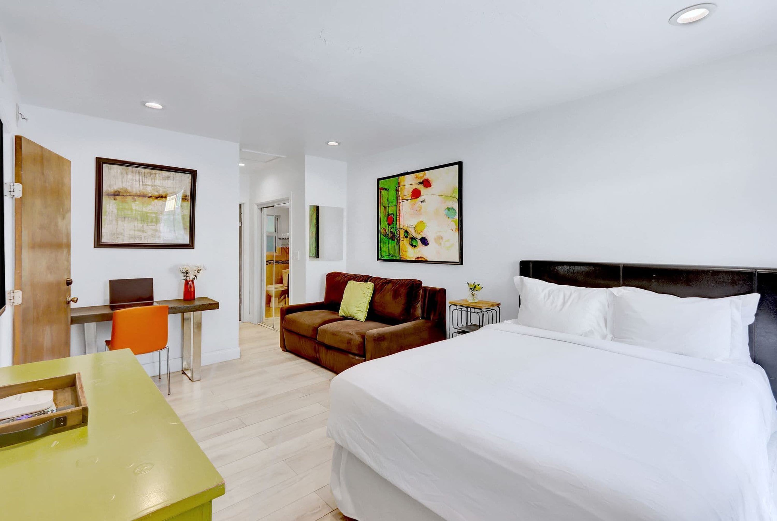 Een hotelkamer met een groot bed, een bureau met stoel, een bank en twee kunstwerken in lijsten aan de muur.