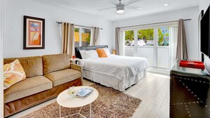Een hotelkamer met een bed, een bank, een televisie en een raam met uitzicht op palmbomen.