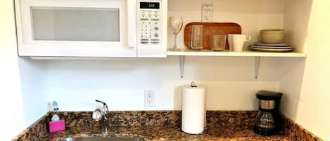 A kitchen with a granite countertop, stainless steel sink, white microwave, and wooden cabinets.