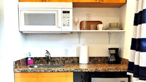 Eine kleine Küche mit Holzschränken, einer Mikrowelle, einer Kaffeemaschine und einem Kühlschrank.
