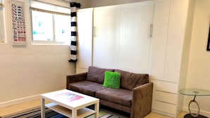 Ein Wohnzimmer mit einem braunen Sofa, einem weißen Couchtisch, einem Streifen Teppich und einem Glastisch mit Metallgestell.