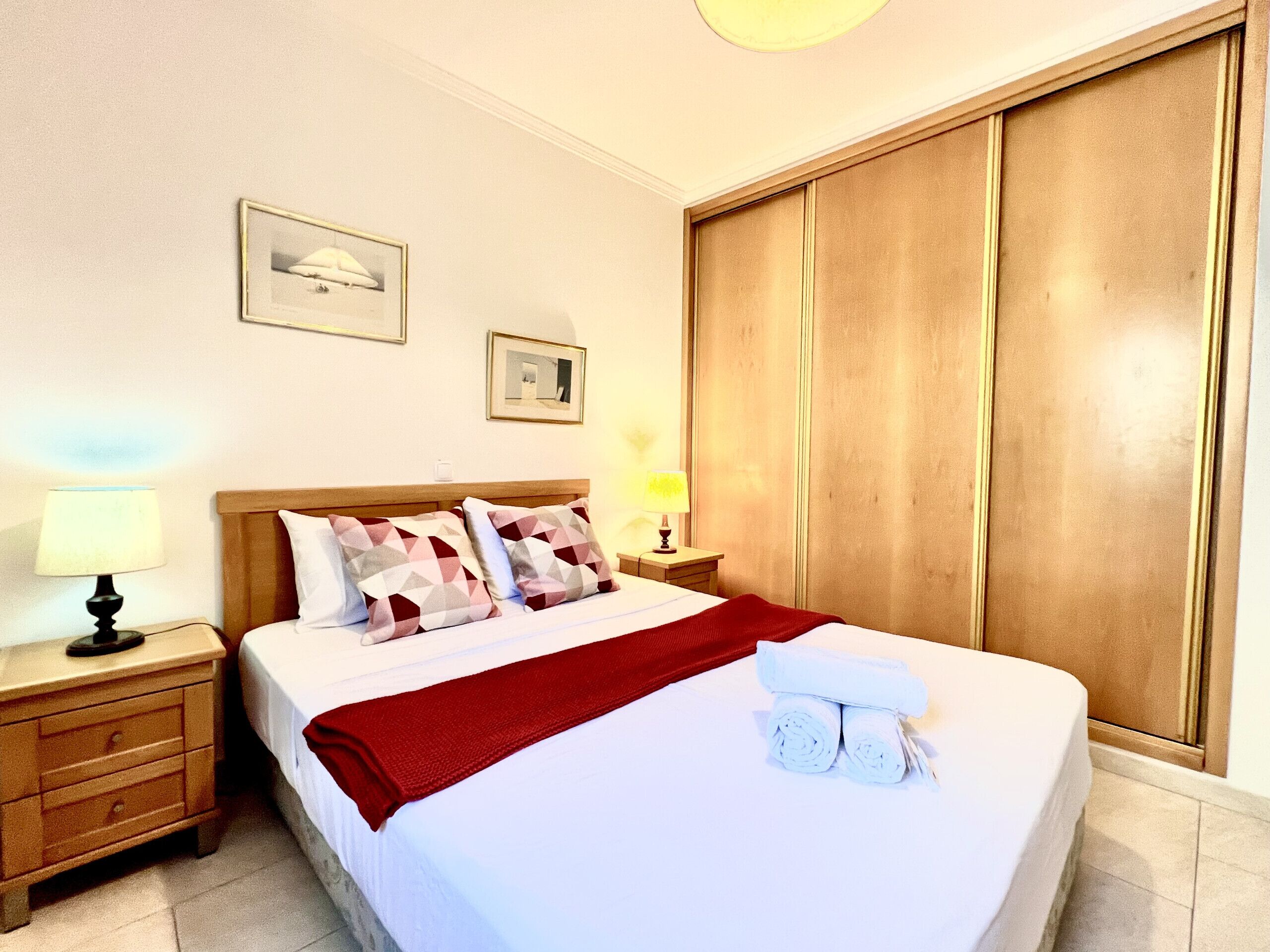 A hotel room with a bed, nightstands, a wardrobe, and two framed pictures on the wall.