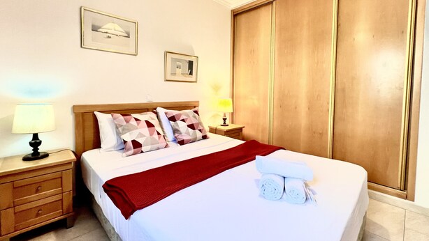 Una habitación de hotel con una cama, mesitas de noche, un armario y dos cuadros en la pared.
