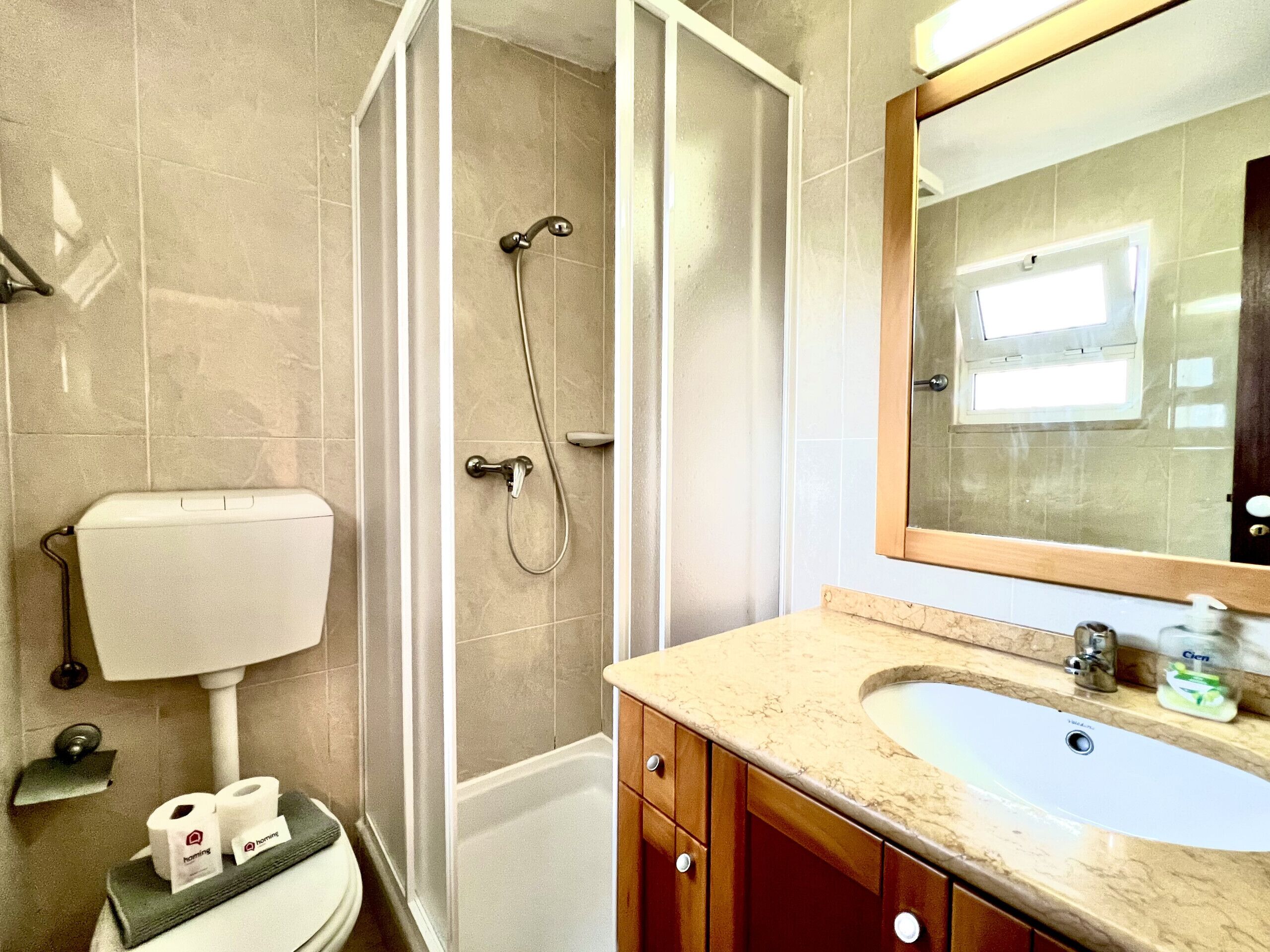 A bathroom with a toilet, shower, sink, and mirror.