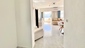 A spacious living area with a sofa, a dining table, and a view of the outside. - Vilamoura SEA Village 2 by Homing (Loulé)
