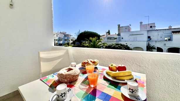 A balcony table with breakfast items, a view of buildings, and a clear sky. - Vilamoura SEA Village 2 by Homing (Loulé)
