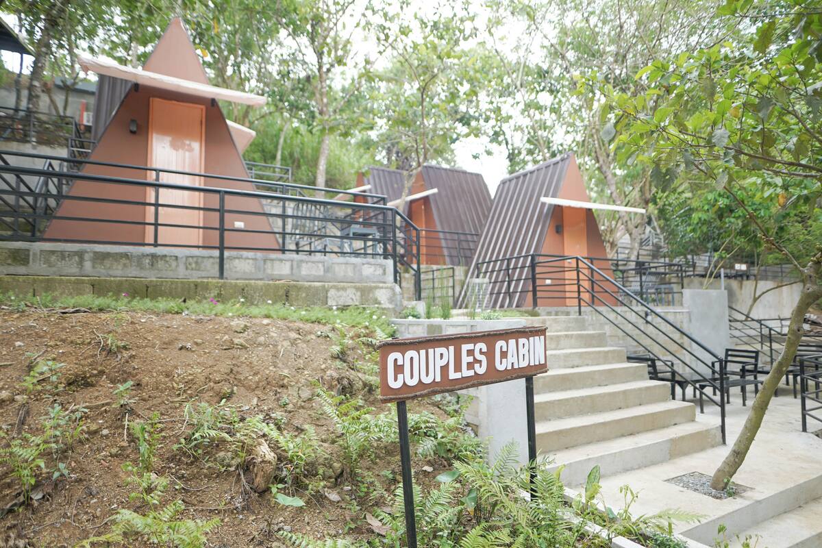 Un panneau indiquant l’emplacement du « Couples Cabin », un escalier menant à un chalet, et la verdure environnante.