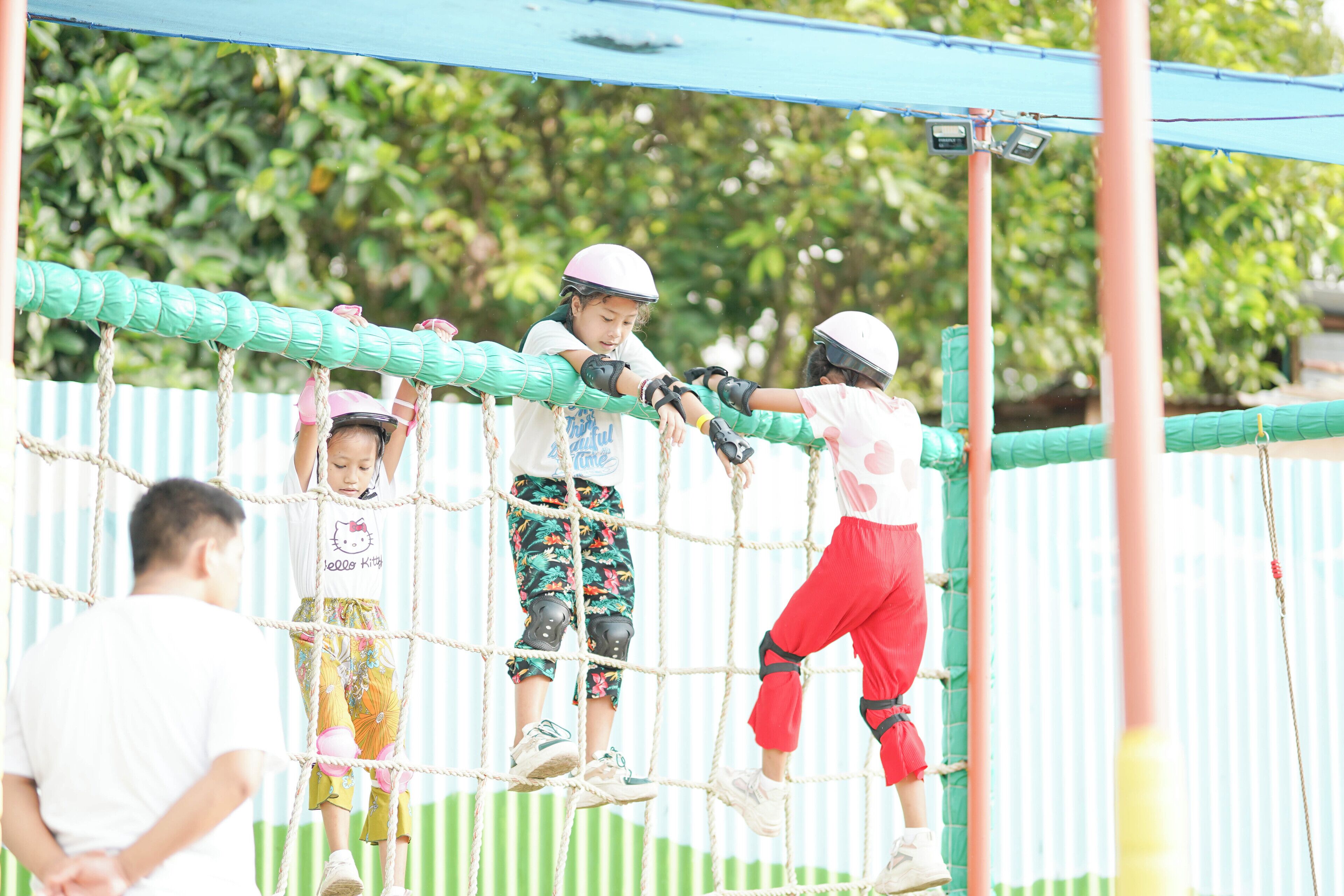 Children playing on a rope bridge in an outdoor setting.