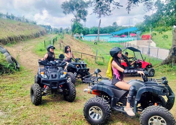 Three people on ATVs on a dirt path with a grassy area and trees in the background. - Ayong's Adventure Park (Silang)