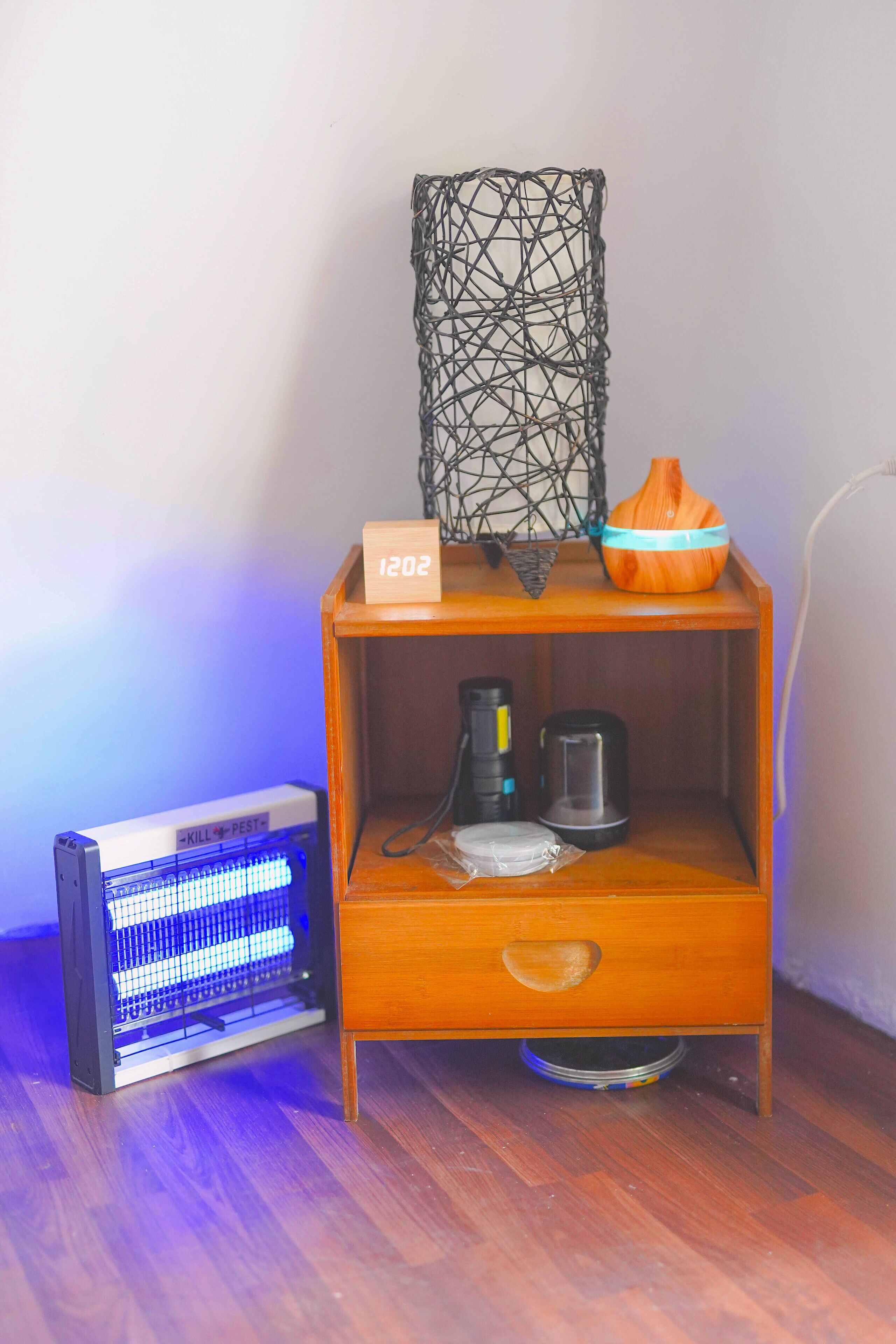 A wooden cabinet with a small shelf, a decorative wire mesh, a wooden bowl, and a kettle.