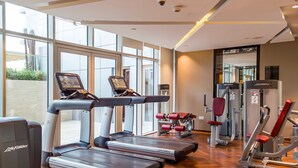 A gym with treadmills, weight machines, and a large window providing natural light. - LUX The Majestine Studio (Dubai)