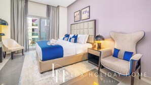 A modern hotel room with a large bed, a chair, a nightstand, and a view of the city. - LUX The Majestine Studio (Dubai)