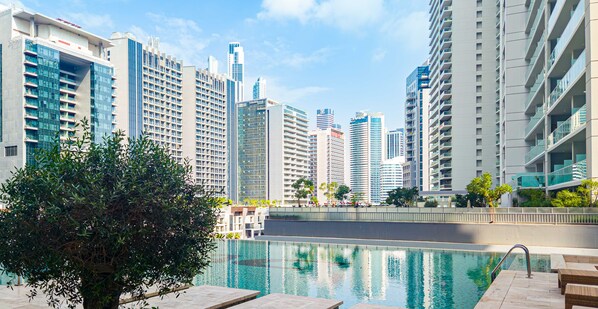 A modern hotel with a pool, surrounded by high-rise buildings and greenery.