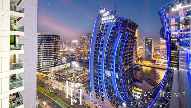 A modern hotel with a curved facade, located in a bustling urban area with a river and other high-rise buildings in the background. - LUX The Majestine Studio (Dubai)