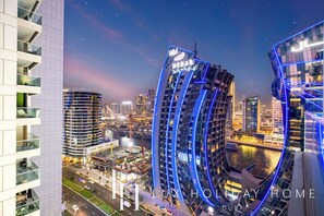 A modern hotel with a curved facade, located in a bustling urban area with a river and other high-rise buildings in the background.