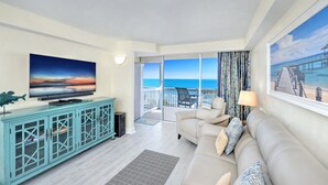 Un salón con televisor, sofá y balcón con vistas al mar.
