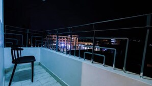 A balcony with a chair, metal railings, and a view of buildings at night.