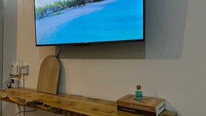 A wooden reception desk with a flat-screen TV displaying a beach scene, a book titled 'The Scarlet Letter', and a small blue bottle.