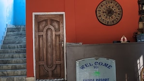 Un comptoir d’accueil avec une pancarte indiquant « Bienvenue à l’Ekora Resort », une porte en bois, une horloge murale décorative et un escalier avec un mur bleu.