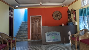Un espace d’accueil avec un sol à carreaux, un comptoir de réception, une porte en bois, un escalier et un ventilateur de plafond.