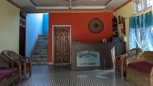 Un espace d’accueil avec un sol à carreaux, un comptoir de réception, des meubles en osier, un escalier et un ventilateur de plafond.