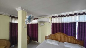 Une chambre d’hôtel équipée d’un lit, d’un ventilateur, d’un climatiseur et d’une chaise en osier.