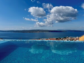 A clear blue sky with clouds, a large body of water, and a tiled infinity pool with a view of a coastal town. - Villa Dolci (Crikvenica)