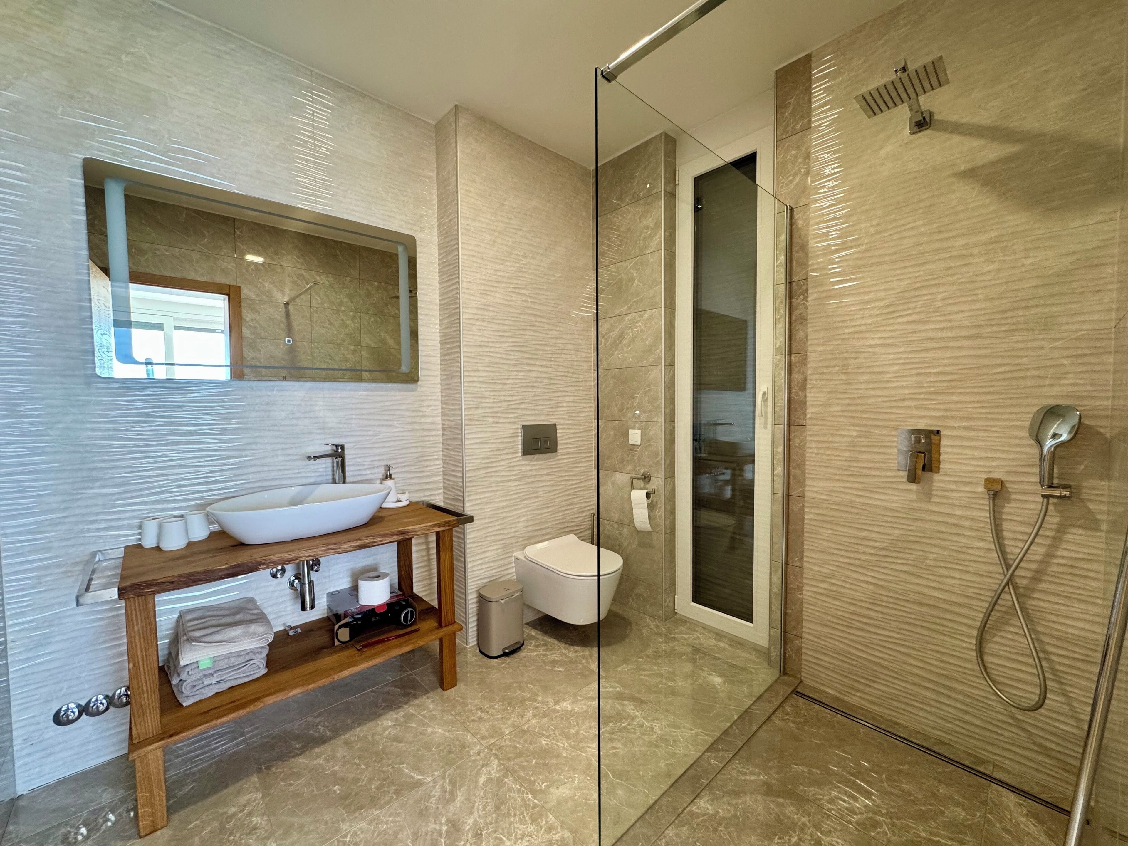 A modern bathroom with a glass-enclosed shower, a wooden vanity with a vessel sink, and a large mirror above the sink.