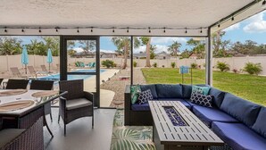 Une terrasse couverte avec une piscine, du mobilier d’extérieur et une vue sur le jardin arrière.