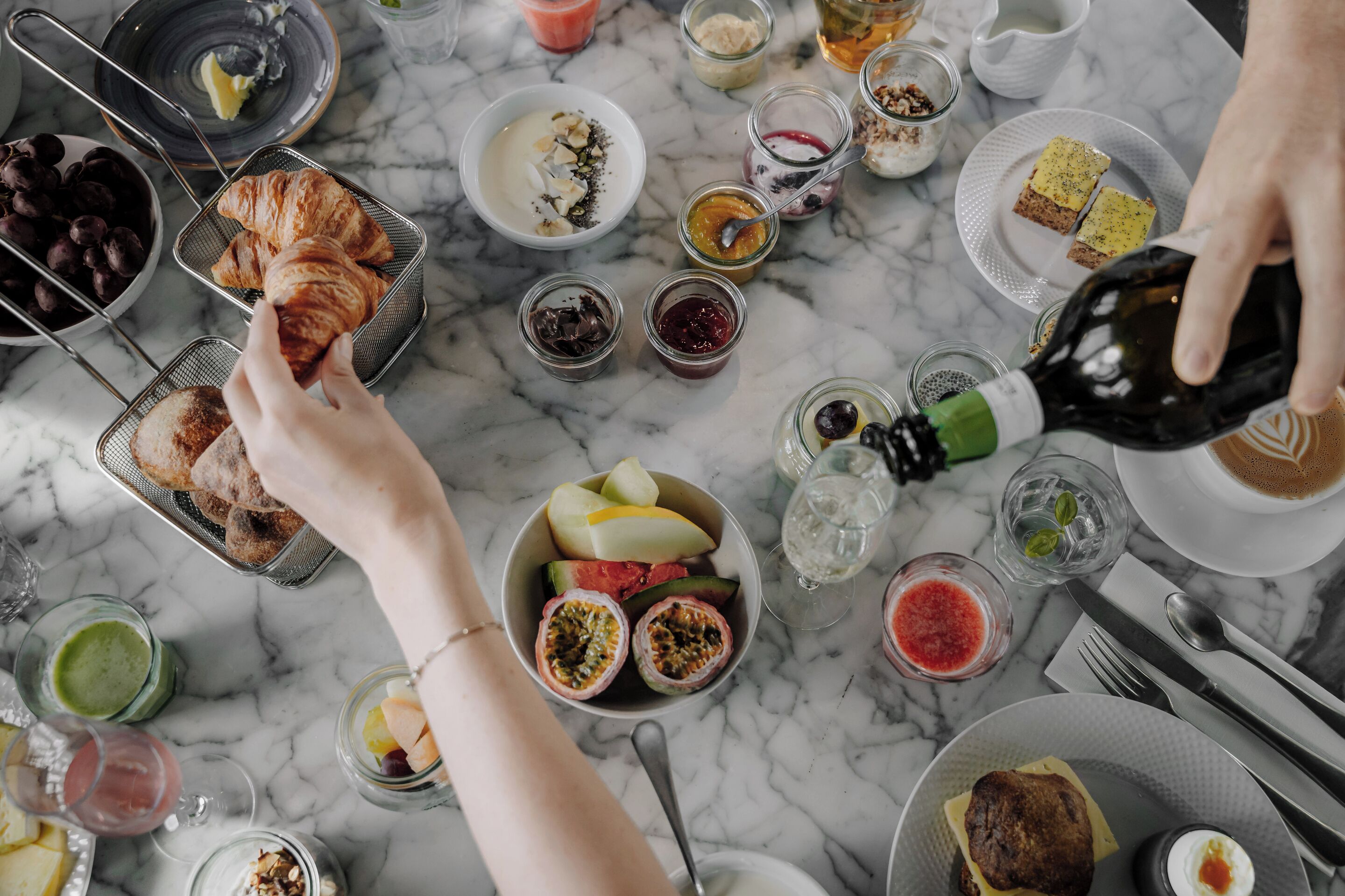 Desayuno con cruasanes, frutas y diversas mermeladas sobre una mesa de mármol.