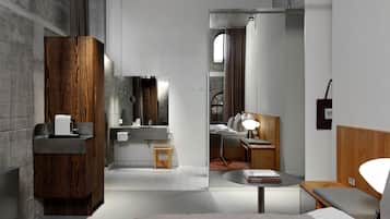 Een moderne hotelkamer met een bed, nachtkastje, lamp en uitzicht op de badkamer.