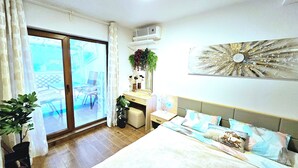 A bedroom with a bed, a desk, a chair, a potted plant, and a view of the outdoors.