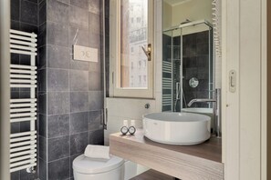 A modern bathroom with a white toilet, a round sink, and a glass shower enclosure. - Modern Studios near the City Centre (Milan)