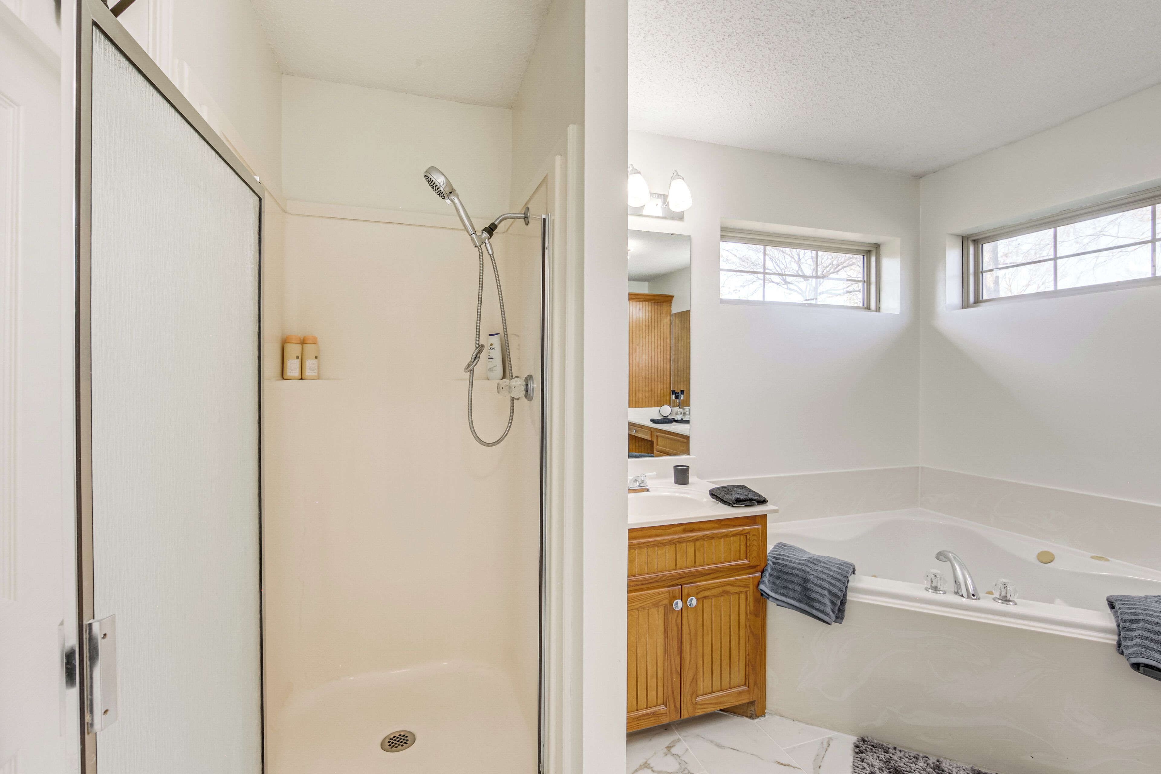 A bathroom with a walk-in shower, a bathtub, wooden cabinets, a vanity with a mirror, and a window providing natural light.