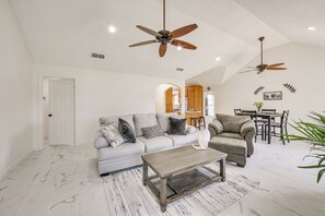 A spacious living room with a grey sofa, a brown armchair, and a coffee table. There are two ceiling fans and a dining area in the background. - 1 Mi to Lake Jacksonville: Pet-friendly Home (Jacksonville)