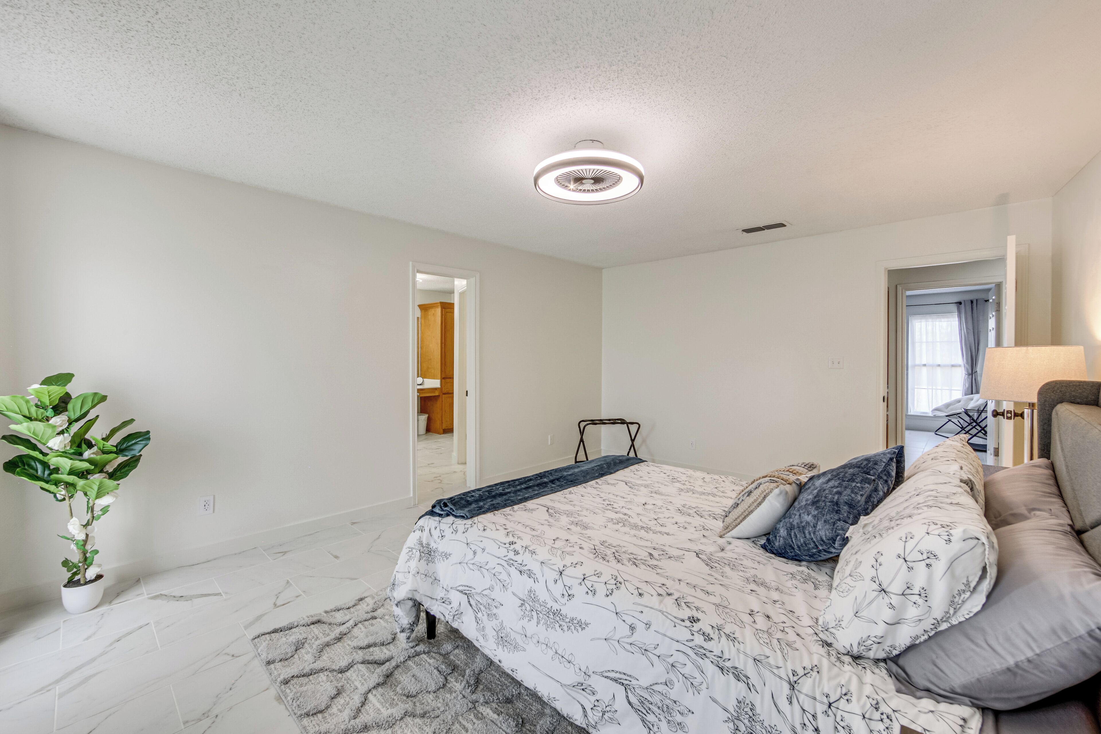 A bedroom with a bed, a plant, a chair, and a lamp.