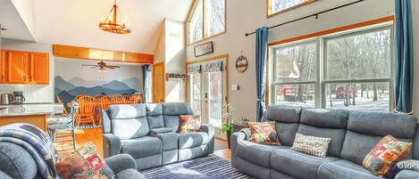 A spacious living room with a sofa set, a dining area with orange chairs, and a kitchen in the background.