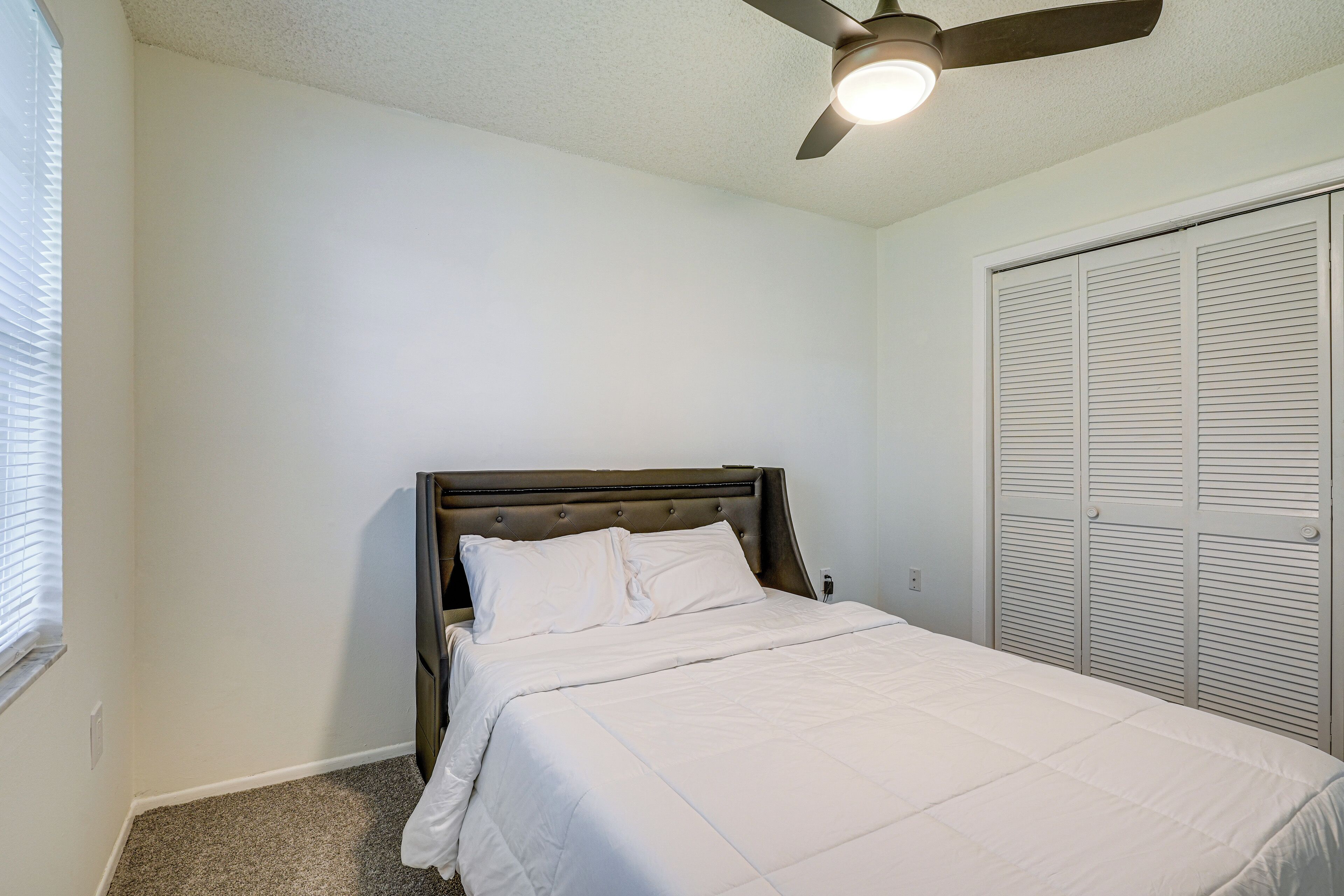 A bedroom with a bed, a ceiling fan, and a closet.