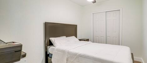 A bedroom with a bed, a ceiling fan, a white door, and a small desk with a printer.