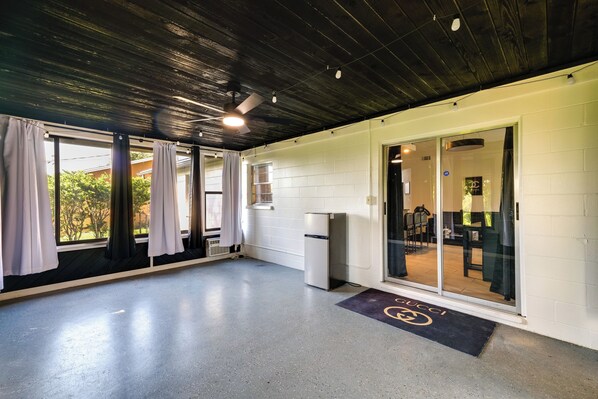 A spacious room with a concrete floor, a ceiling fan, a refrigerator, and a large sliding glass door leading to a dining area.