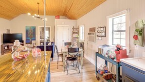 A spacious kitchen with wooden cabinets, a dining area with a table and chairs, a large window, and a TV in the background. - Large Yard + Pond: Fayetteville Rural Retreat (Fayetteville)