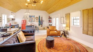 A spacious living area with a wooden ceiling, a leather sofa, a round ottoman, and a dining area with a red refrigerator. - Large Yard + Pond: Fayetteville Rural Retreat (Fayetteville)