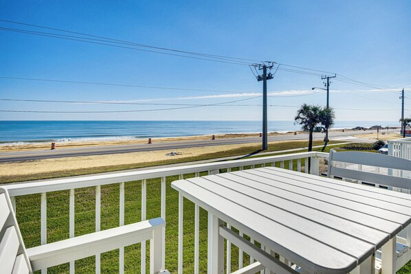 A beach view from a balcony with a white railing, a palm tree, and a clear sky. - Walk to Ocean: Family Retreat in Ormond Beach! (Ormond Beach)