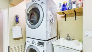 A laundry area with stacked washers and dryers, a drying rack, and a sink with a mirror. - Walk to Ocean: Family Retreat in Ormond Beach! (Ormond Beach)