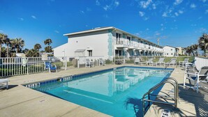 A swimming pool with a 5 ft 6 in depth marker, surrounded by lounge chairs and a white building with balconies. - Walk to Ocean: Family Retreat in Ormond Beach! (Ormond Beach)