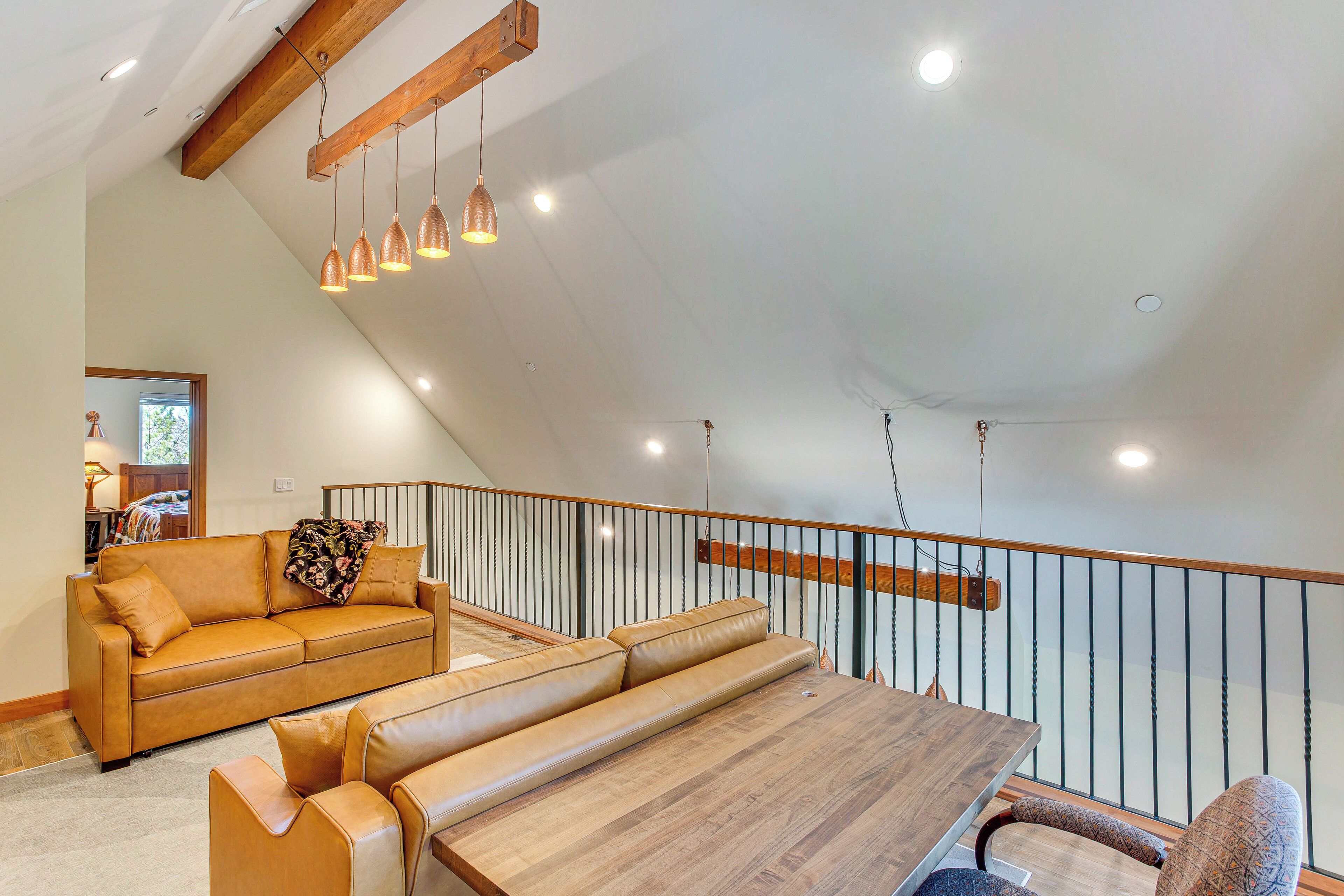 A spacious loft with a high ceiling, a wooden dining table, leather sofas, and pendant lighting.