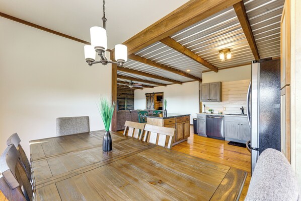 A spacious dining area with a wooden table and chairs, a chandelier, and a view into the kitchen with modern appliances.